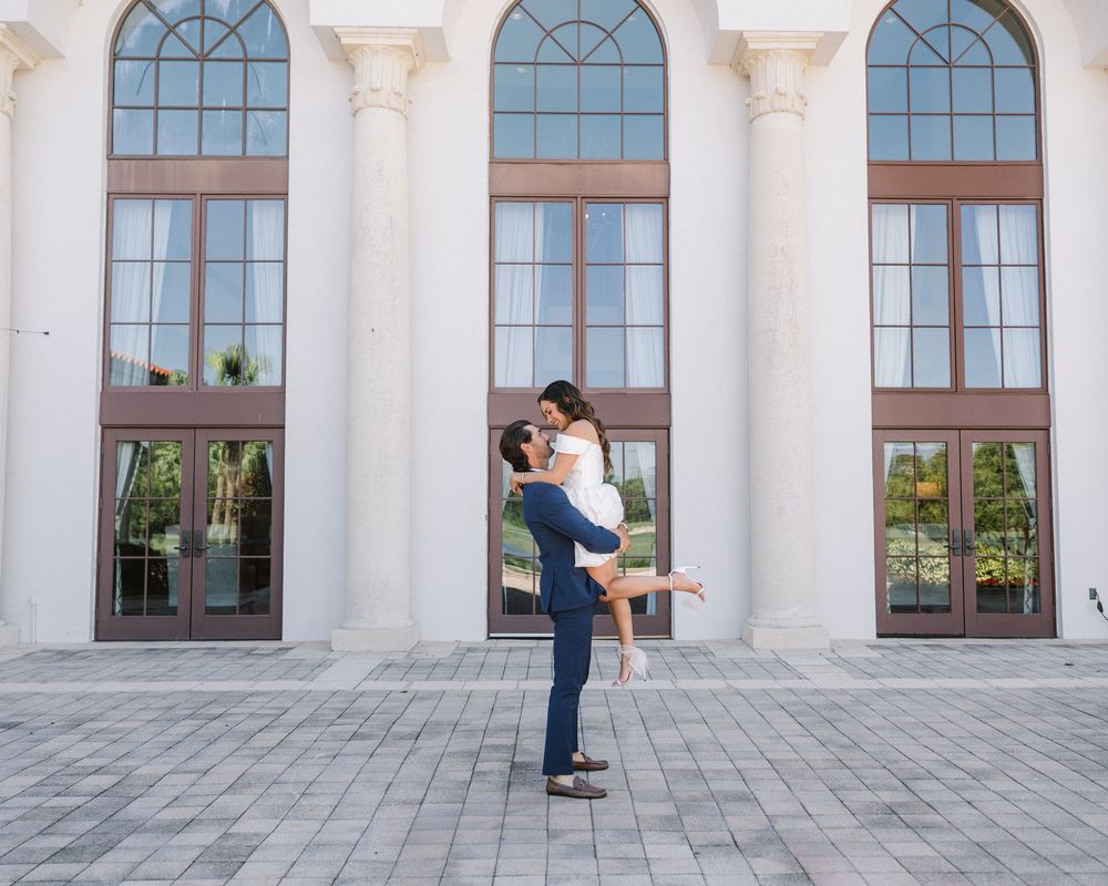 Couple celebrating their love in front of a grand building with arched windows.
