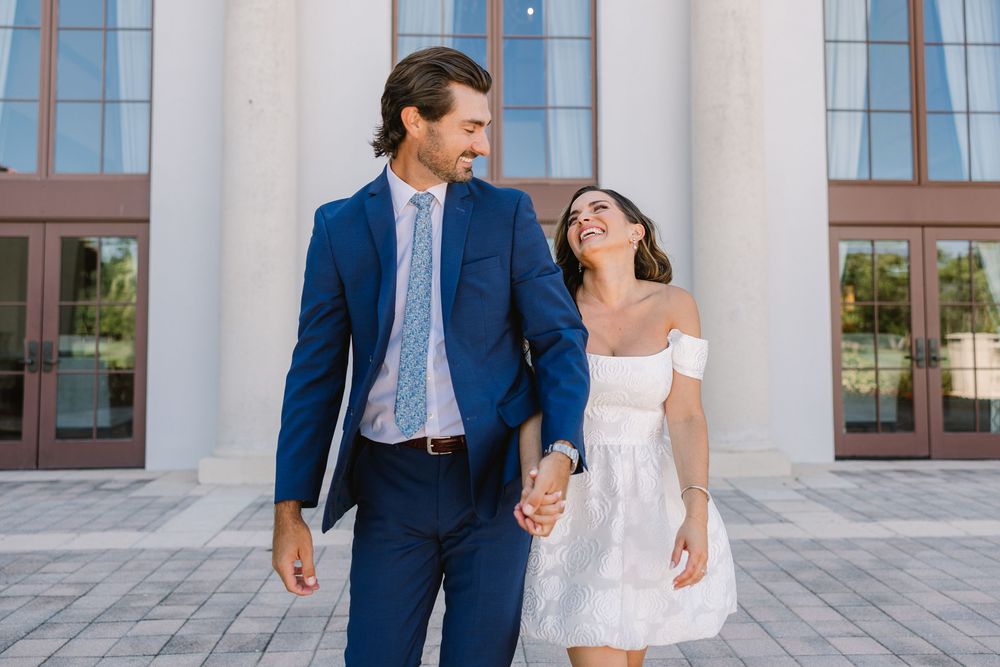 Couple walking hand in hand in front of a classical building with white columns.