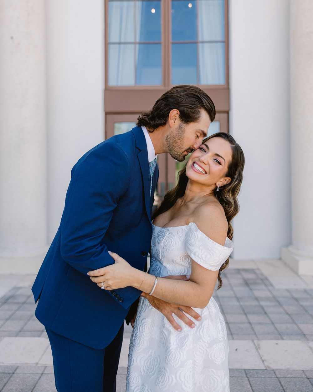 Sweet moment shared between a couple in formal attire against white columns.