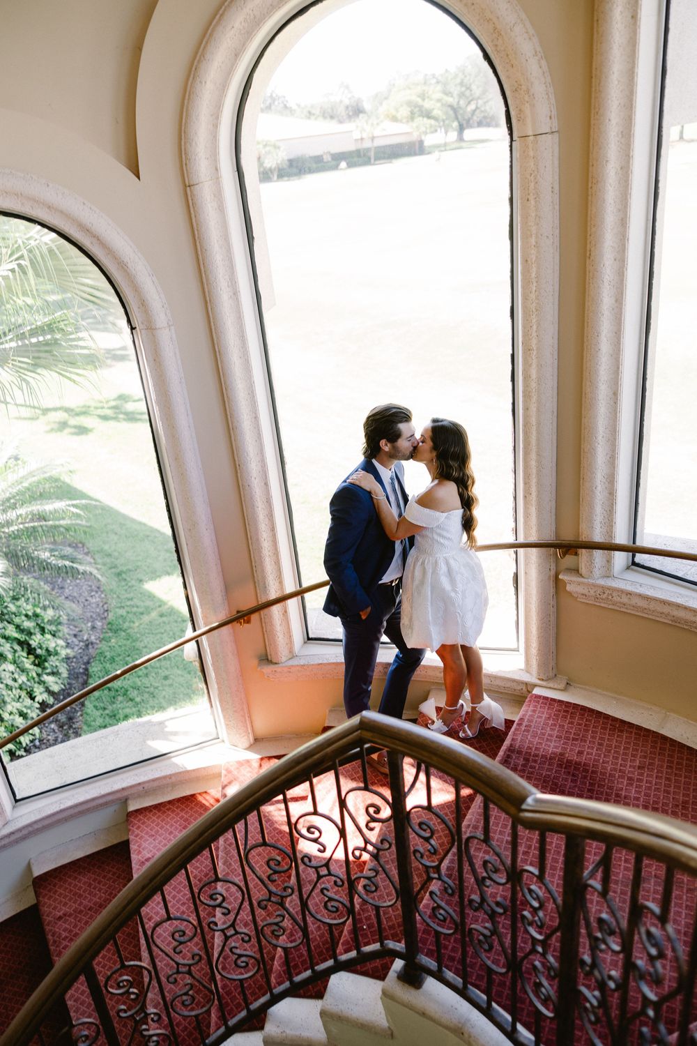 Romantic moment on an elegant curved staircase with arched windows.