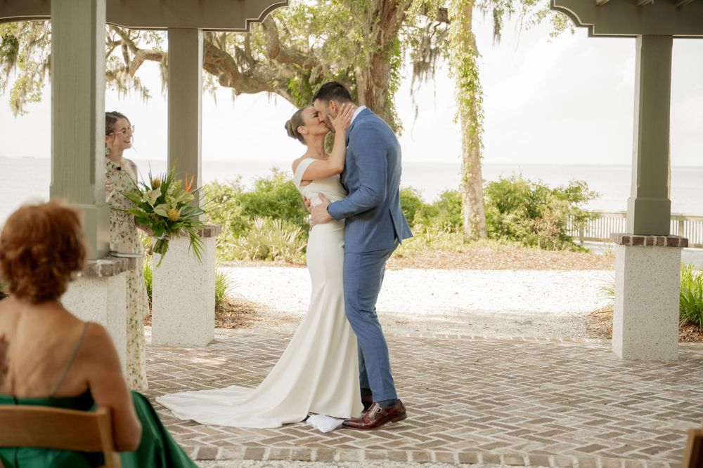 A romantic outdoor wedding ceremony under a covered pavilion with palm trees and natural light.