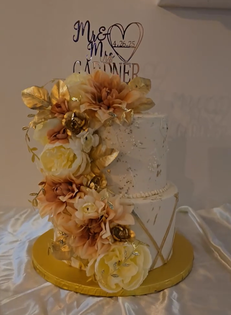 Elegant white three-tier wedding cake decorated with gold and peach flowers on a gold base with Mr and Mrs topper.