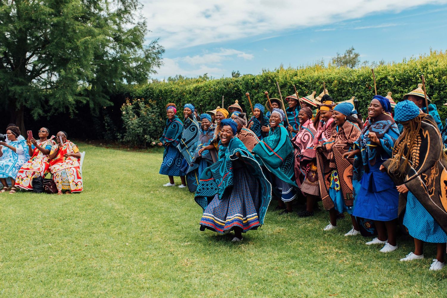 A group of vibrant dancers in traditional clothing form a circular arrangement during a cultural outdoor performance.