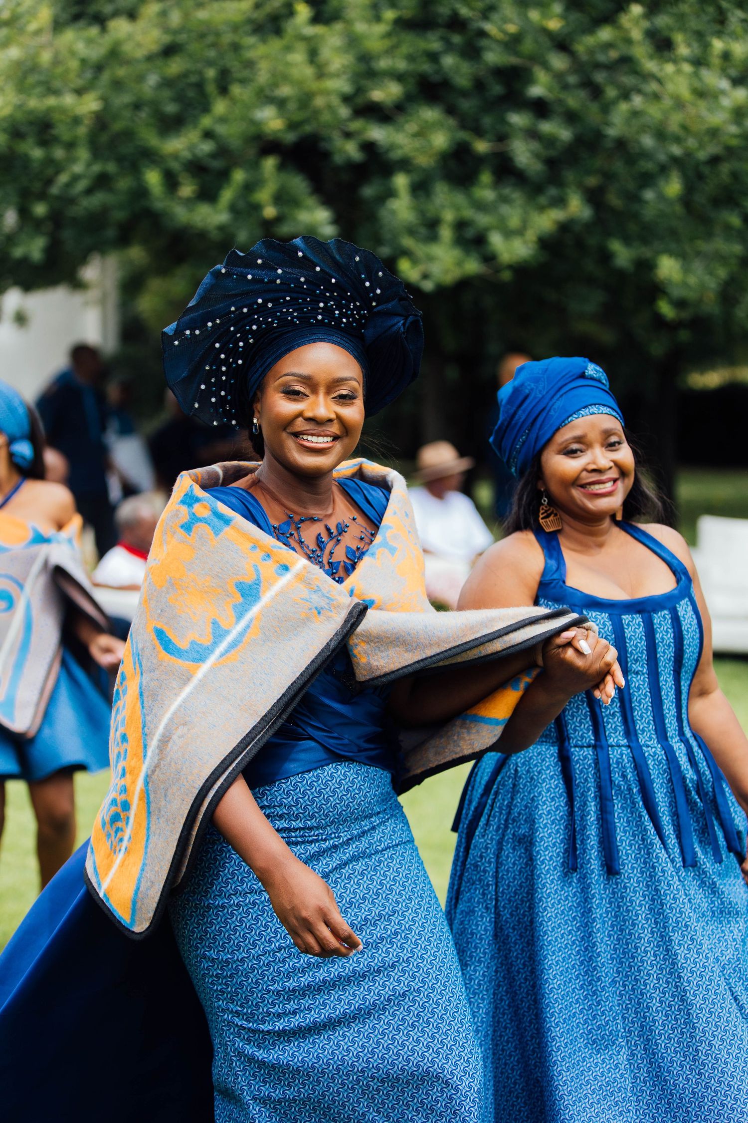 Traditional celebration with people wearing vibrant blue Shweshwe dresses and head wraps at an outdoor gathering.