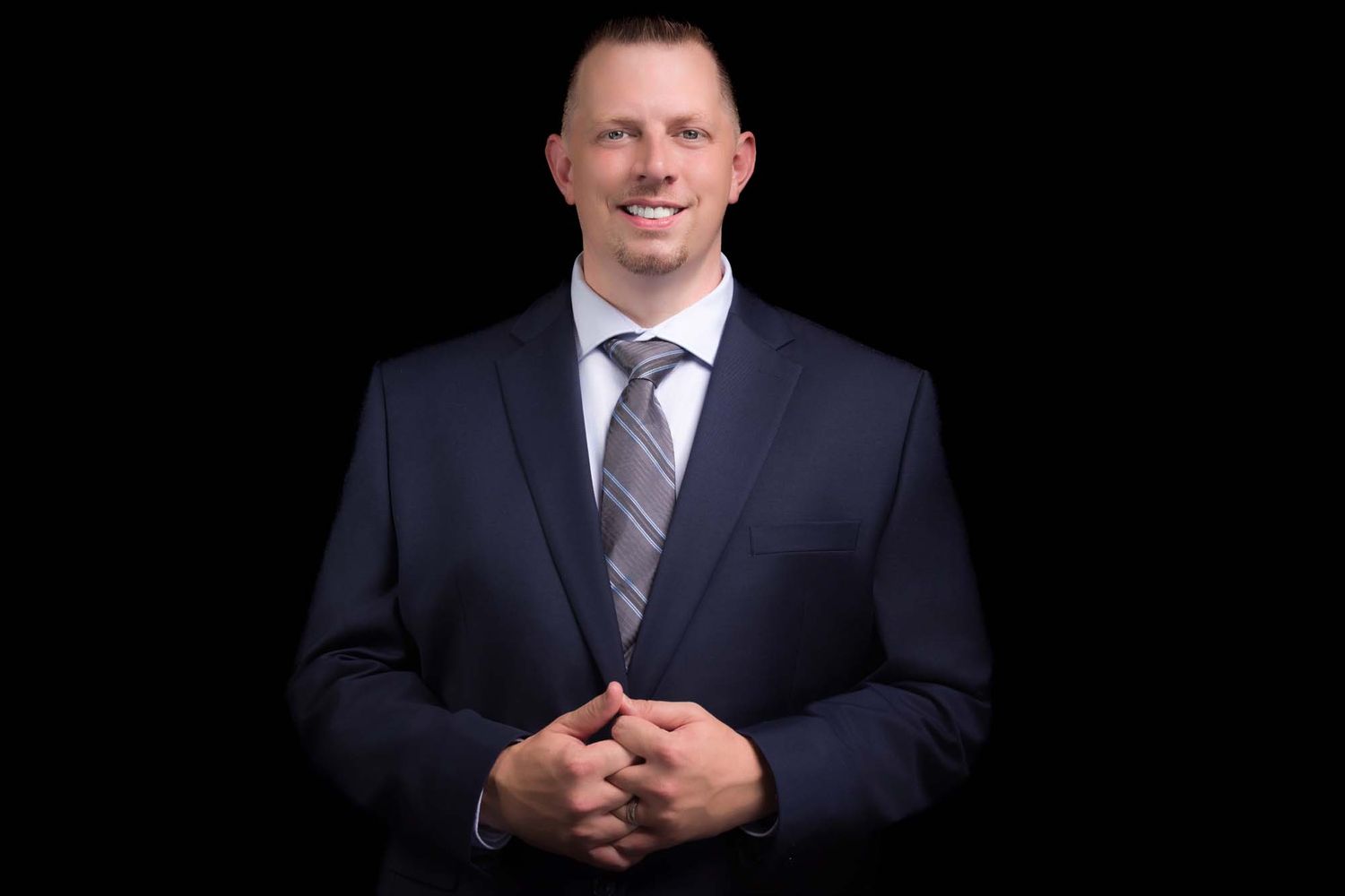 Professional studio headshot portrait of person in a dark business suit against black background.