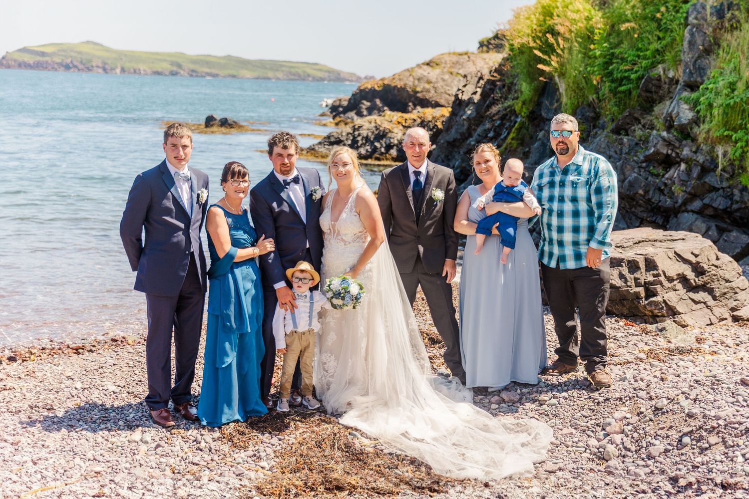 Wedding party gathers along a scenic rocky beach coastline during a seaside celebration ceremony.