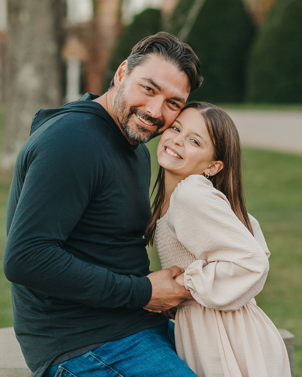 A couple in coordinating navy and cream sweaters embrace and smile outdoors in a natural setting.