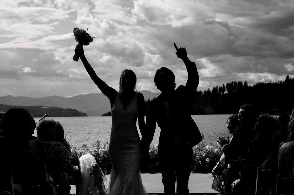 Silhouettes of a celebration by a lake with mountains in the background under dramatic cloudy skies.