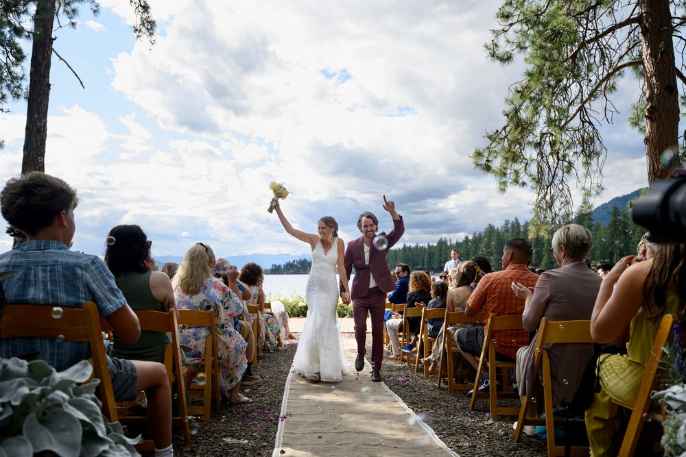 Outdoor wedding ceremony guests seated in wooden chairs overlooking a scenic mountain landscape in summer.