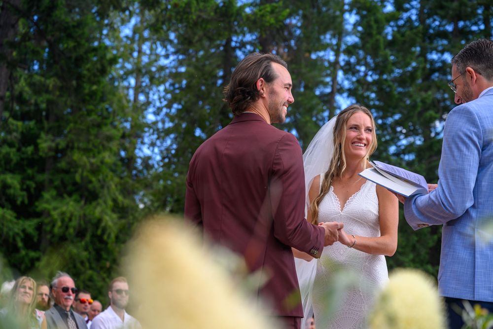 Outdoor summer wedding ceremony taking place in a lush garden setting with green trees in the background.