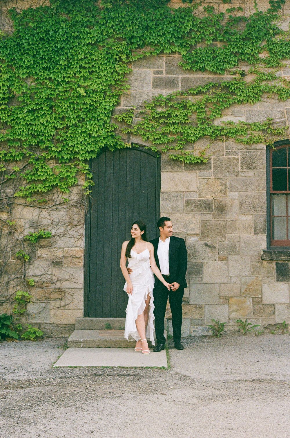 A couple poses against an ivy-covered stone wall for an artistic wedding photoshoot.