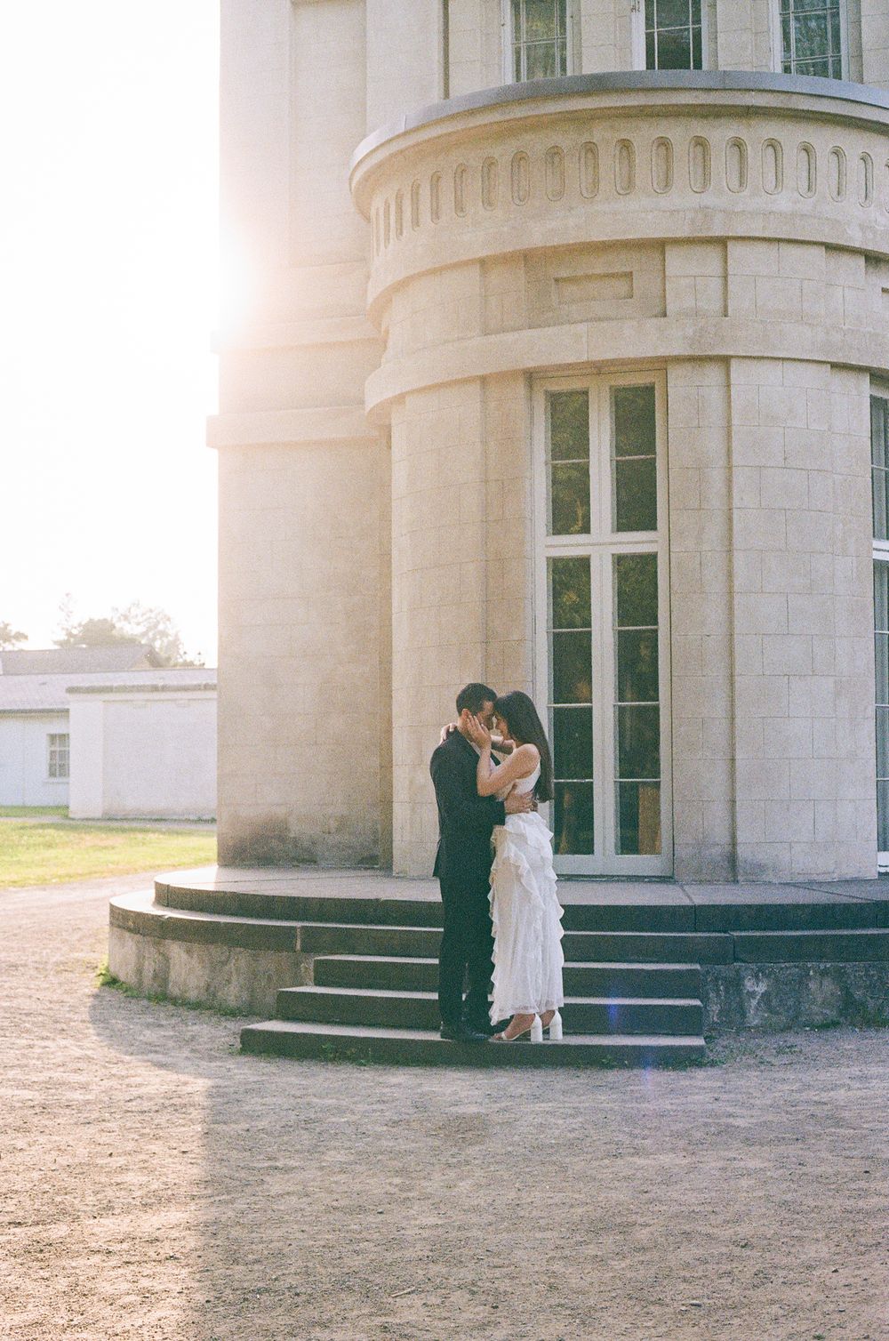 Romantic couple sharing an intimate moment against a stone building at sunset.