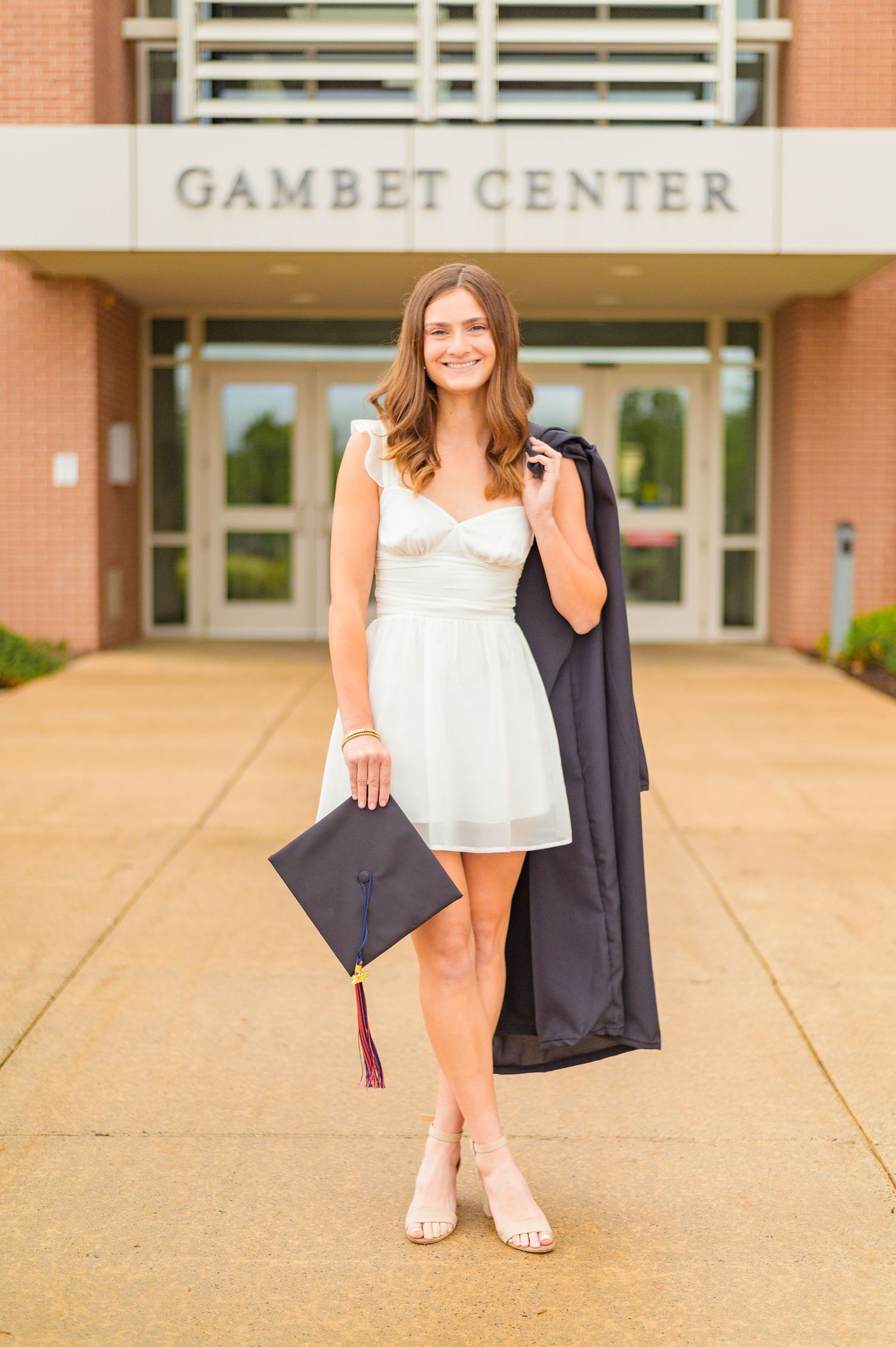Graduate poses with cap and gown outside Gambet Center building.