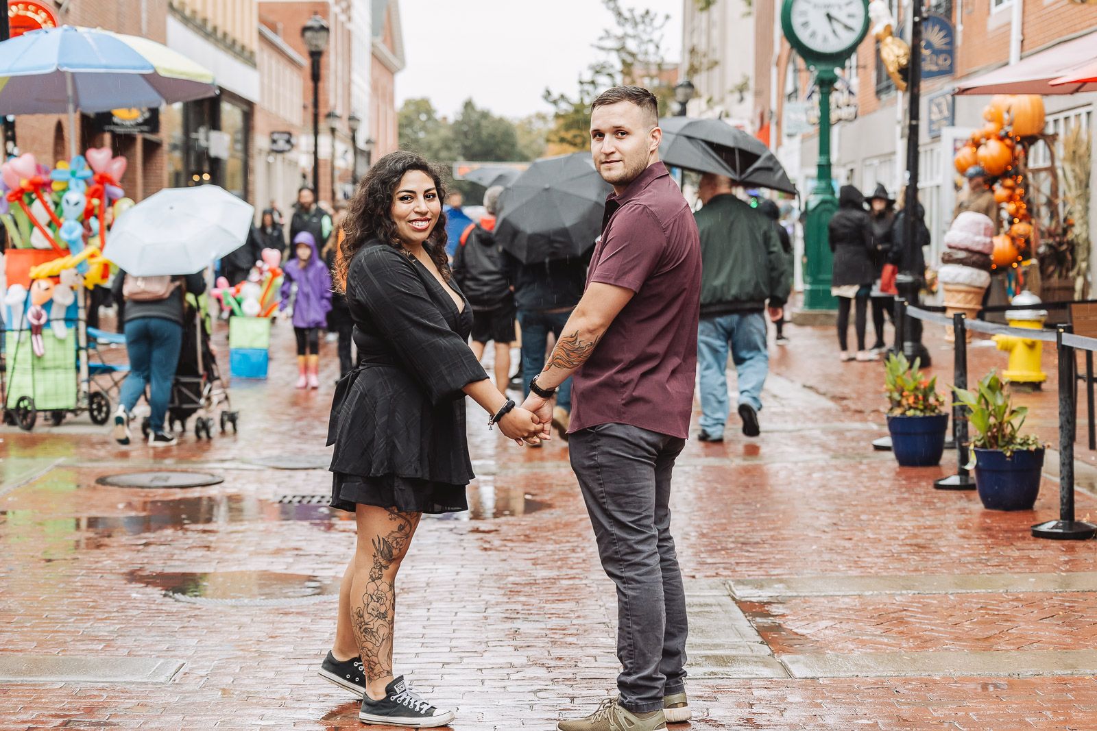 Couple holding hands while standing on wet cobblestone street near local shops.