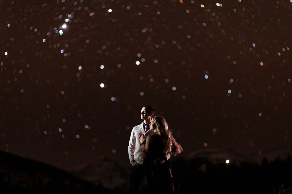 A couple stands close together under a starry night sky creating a romantic silhouette against the dark backdrop by Sofia Katherine.
