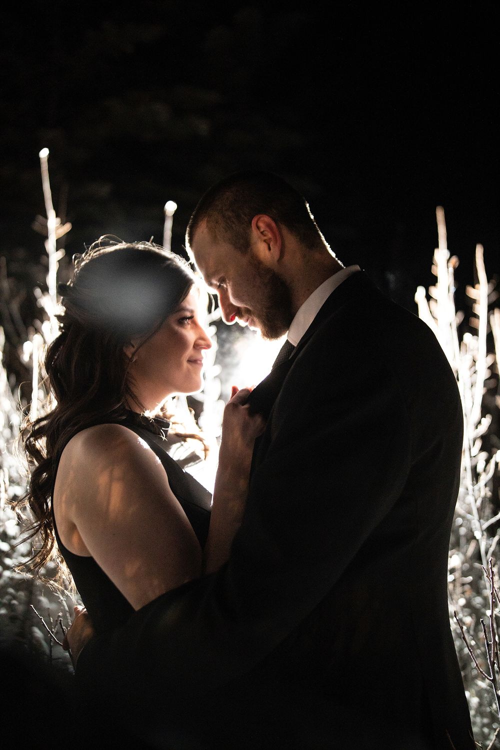 A romantic couple in formal attire share an intimate moment surrounded by glowing sparklers in the darkness by Sofia Katherine Photography.