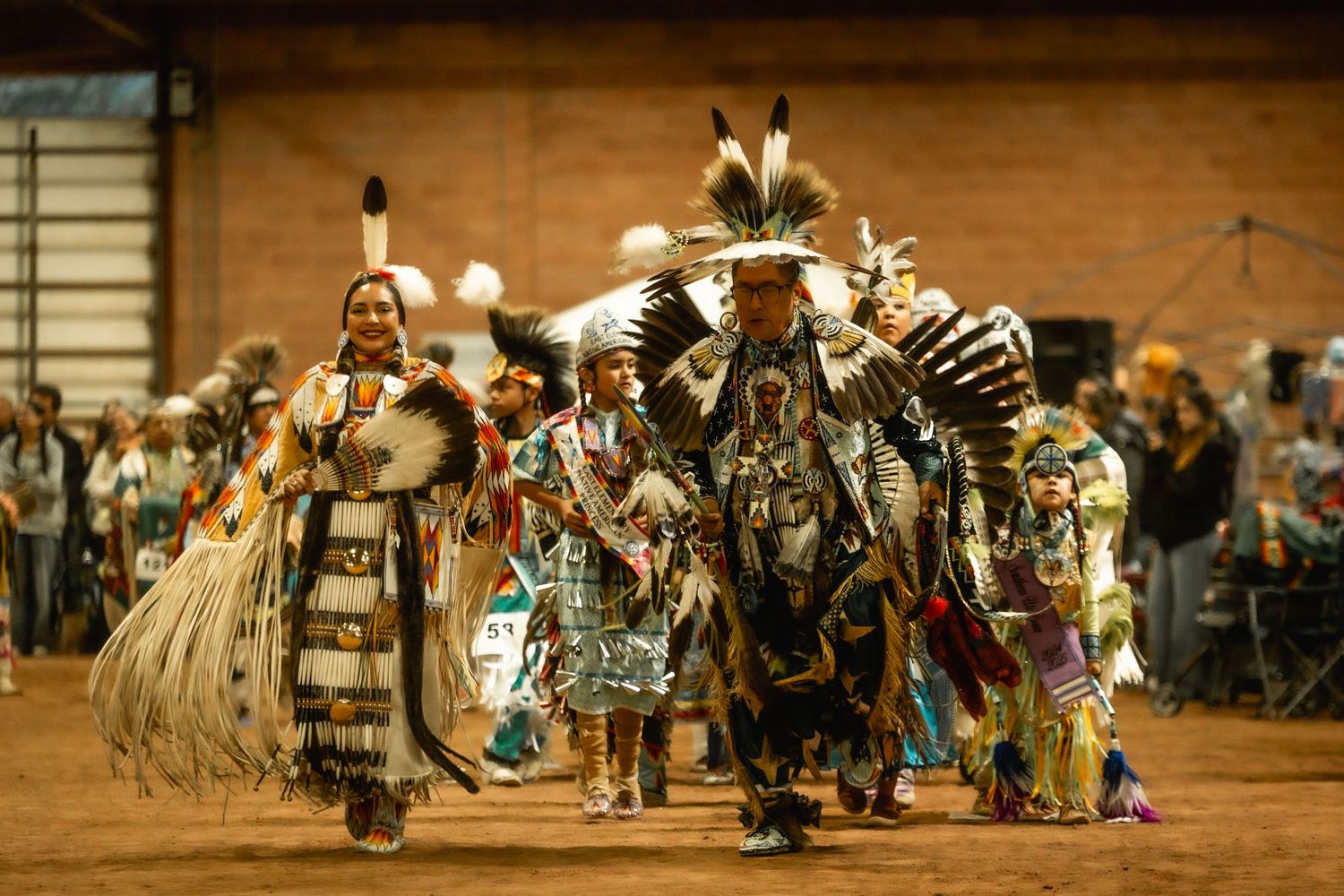 Native American dancers performing traditional dances in regalia at an indoor powwow.