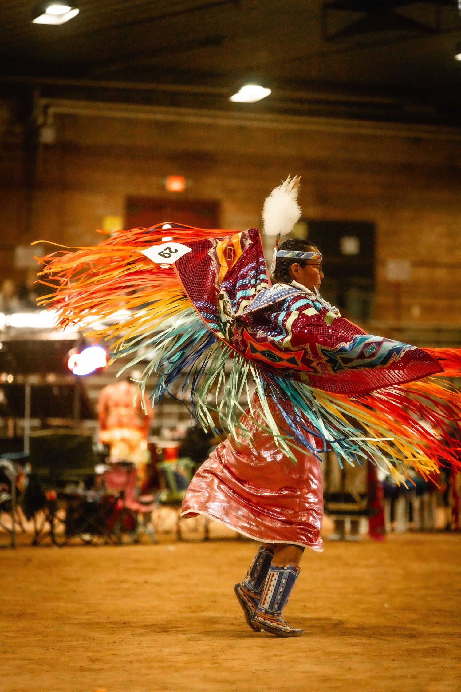 Traditional dancer in vibrant regalia performing dynamic movements at a powwow.