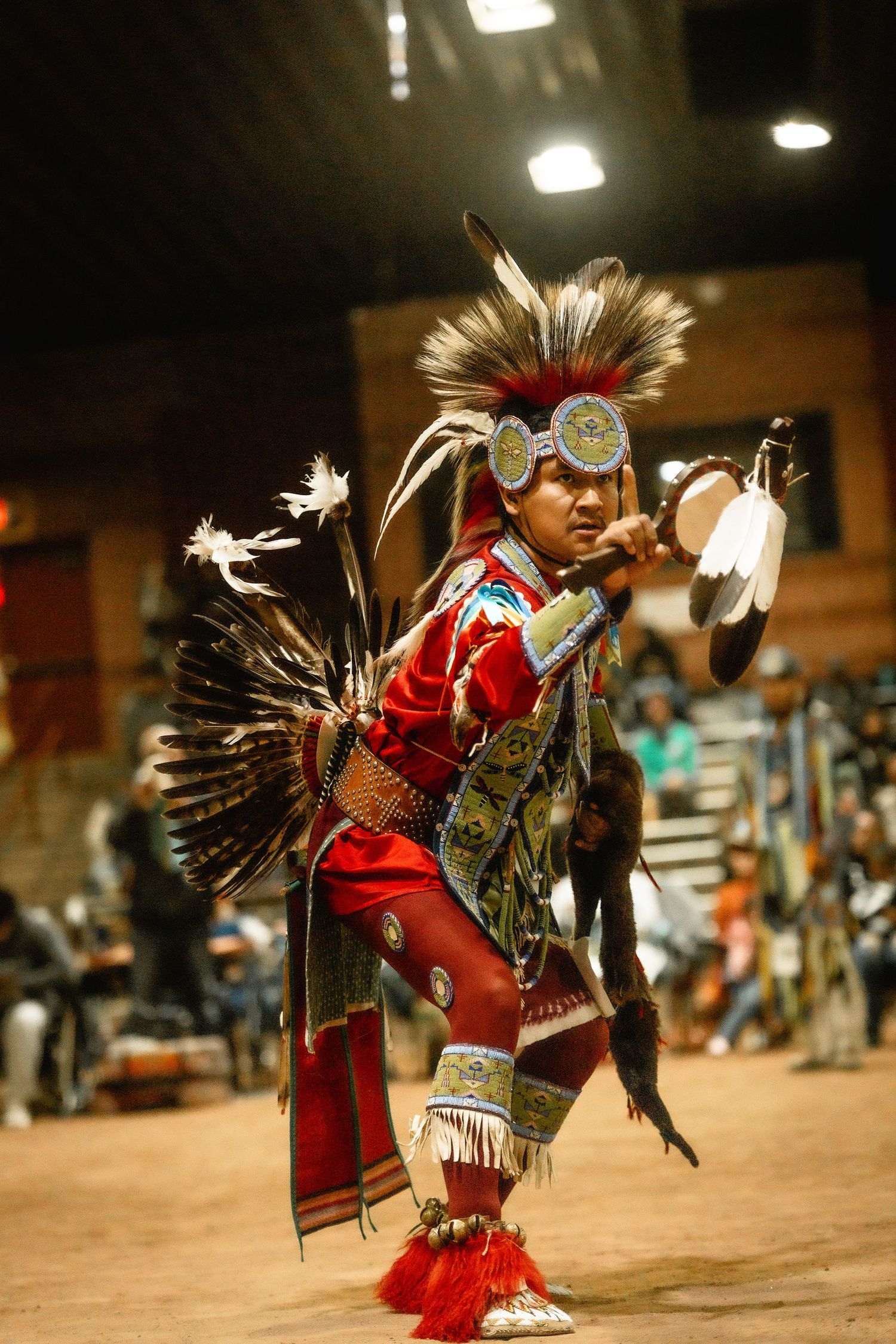Native American dancer in red regalia and feathered headdress performing traditional movements.