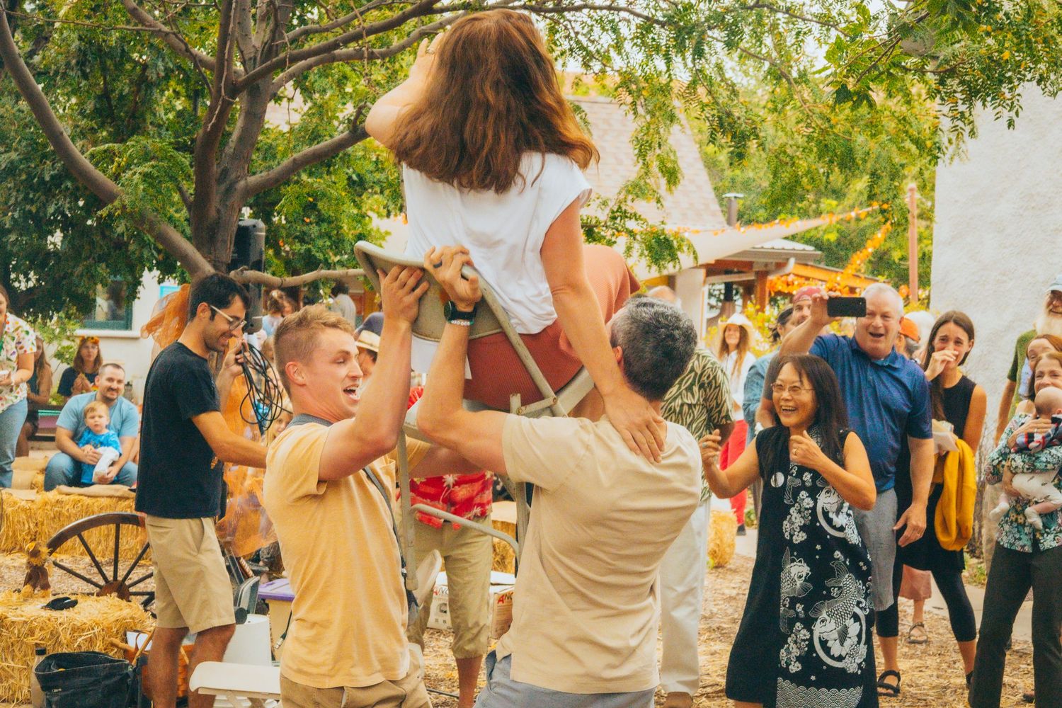 Joyful crowd scene at an outdoor summer celebration with people lifting and dancing.