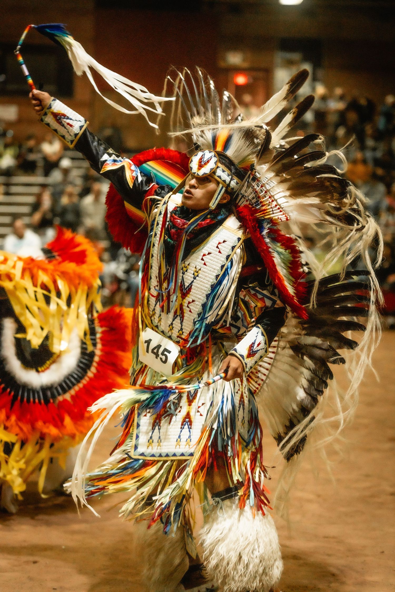 Colorful feathers and regalia create motion blur during an energetic Native American dance performance.