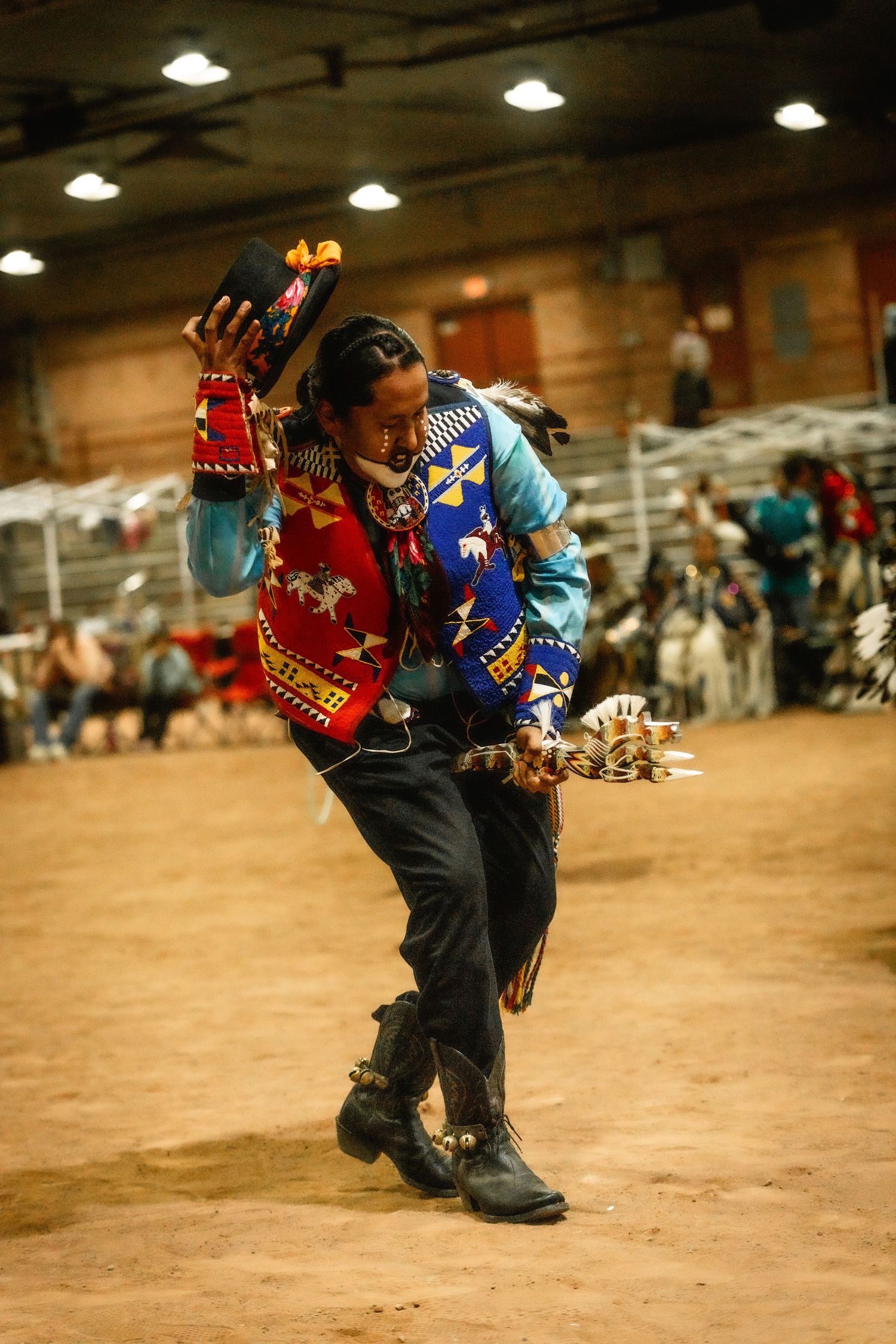 Two dancers in traditional regalia perform expressive movements at an indoor pow wow gathering.