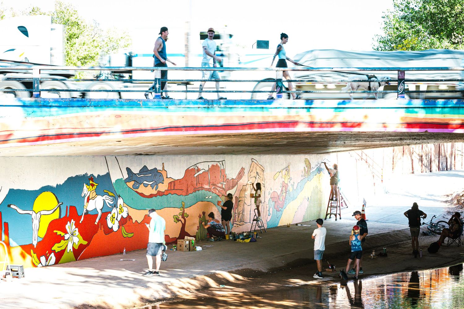 Urban art mural under bridge with people walking and taking photos.