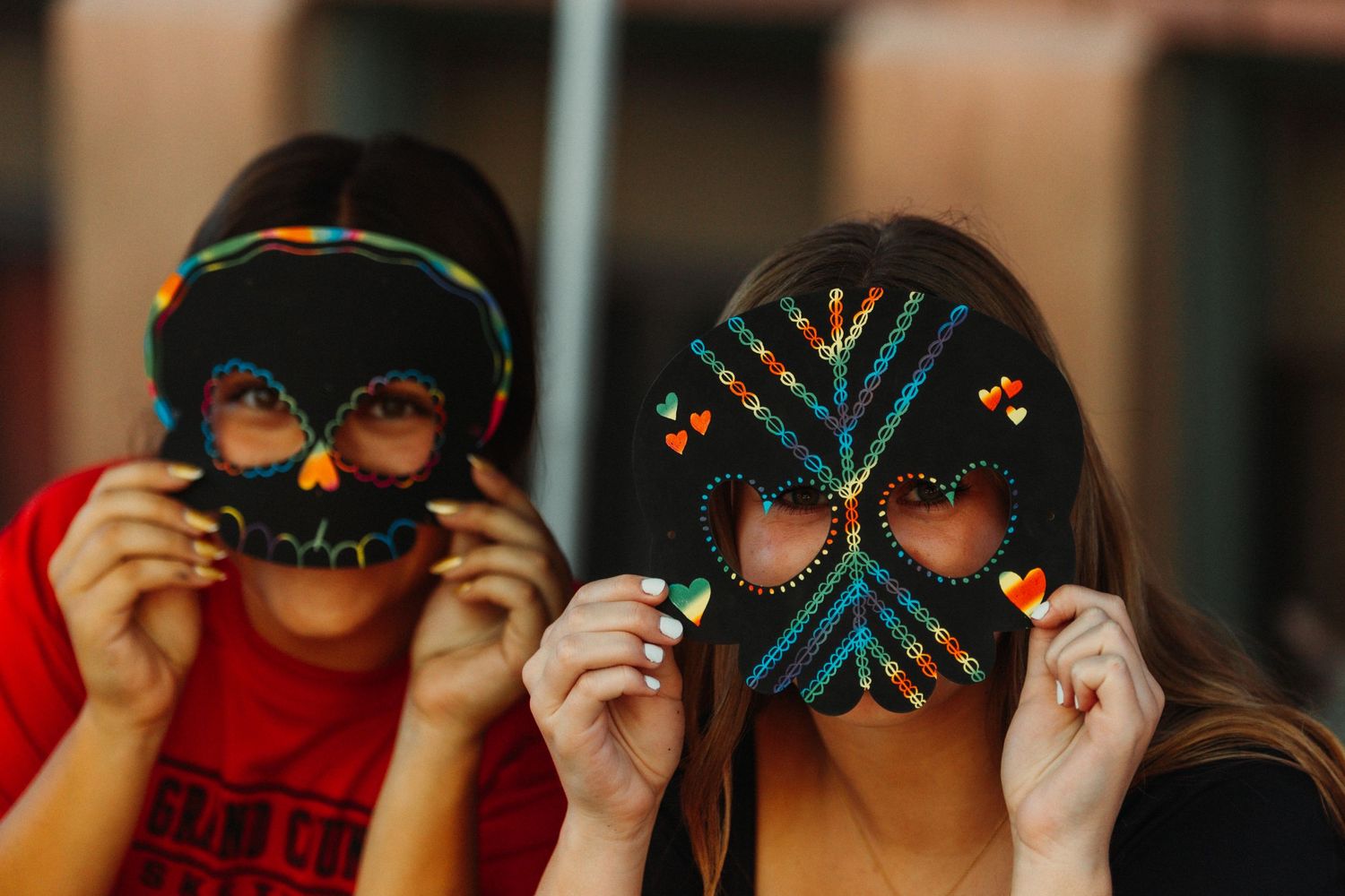 Two people holding decorated masks over their faces in playful pose.
