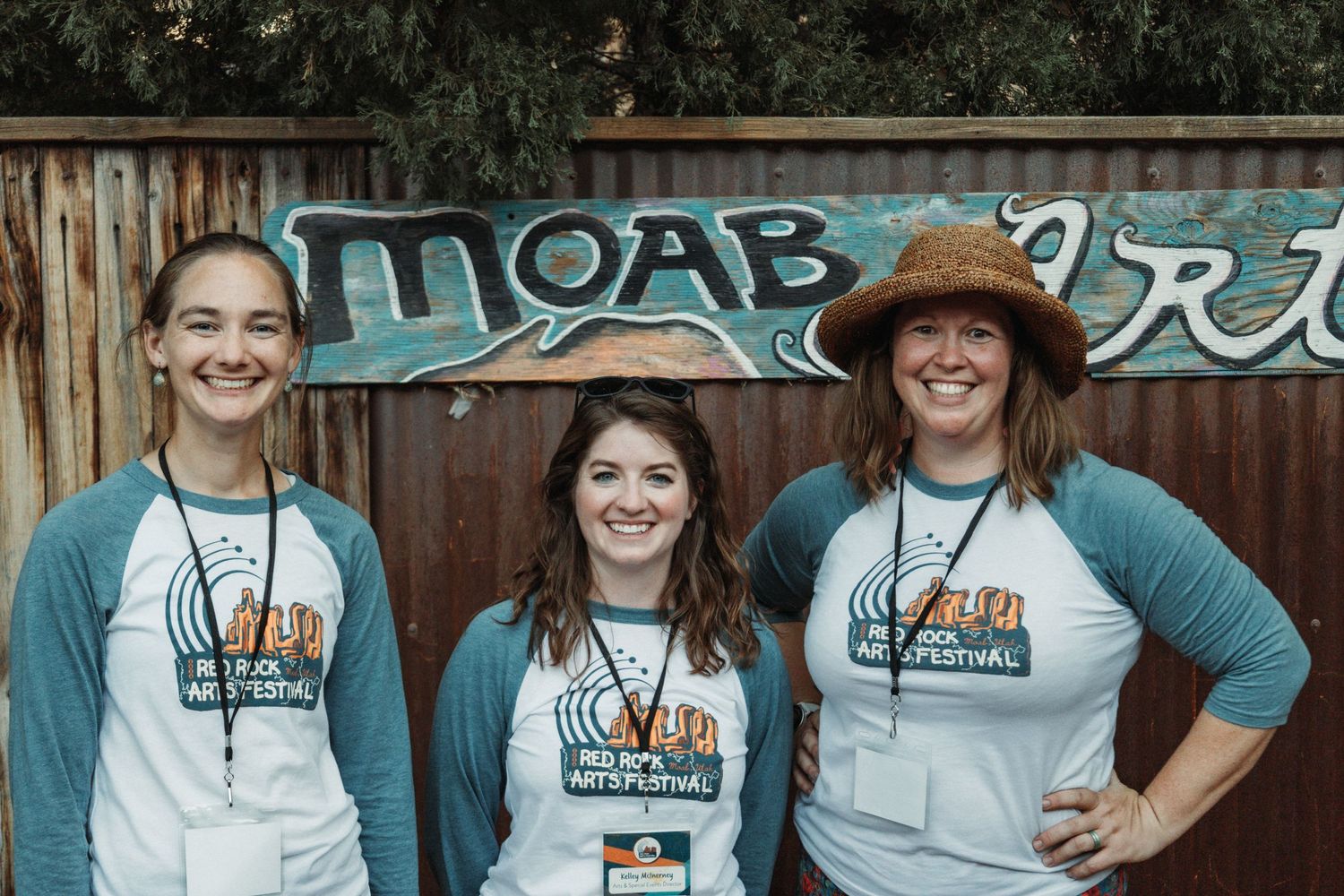 Three staff members wearing matching festival t-shirts pose together.