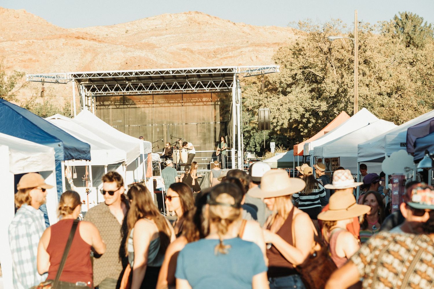 Outdoor festival crowd scene with tents and sunny skies in the background.