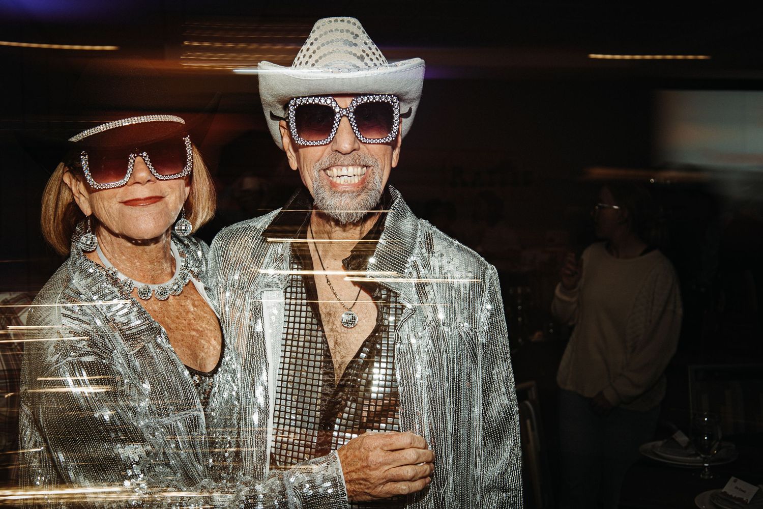 Party-goers in matching silver disco outfits and cowboy hats pose at a nighttime event.