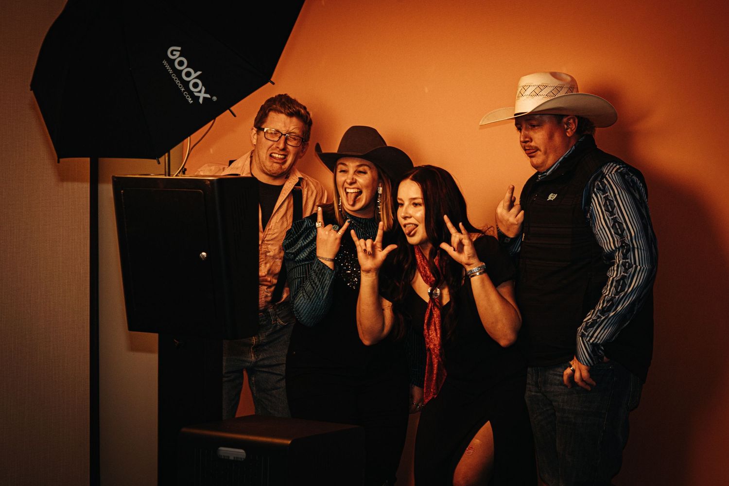 People pose and interact playfully against a warm orange backdrop during an event.