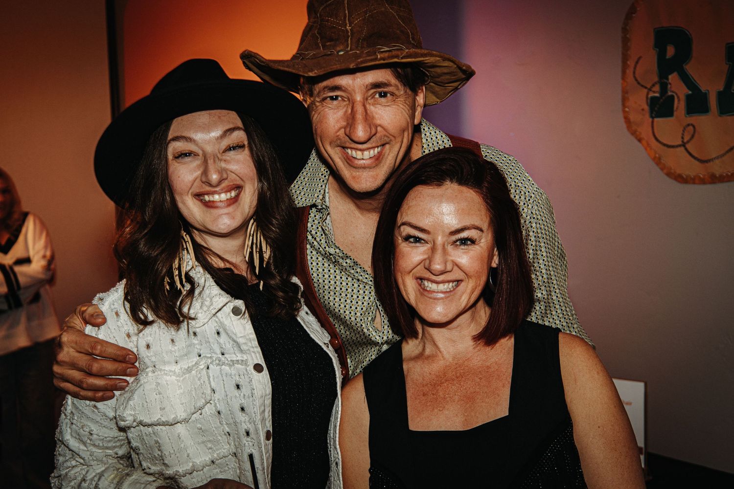 Group of friends in western attire smile and pose together at a social gathering.
