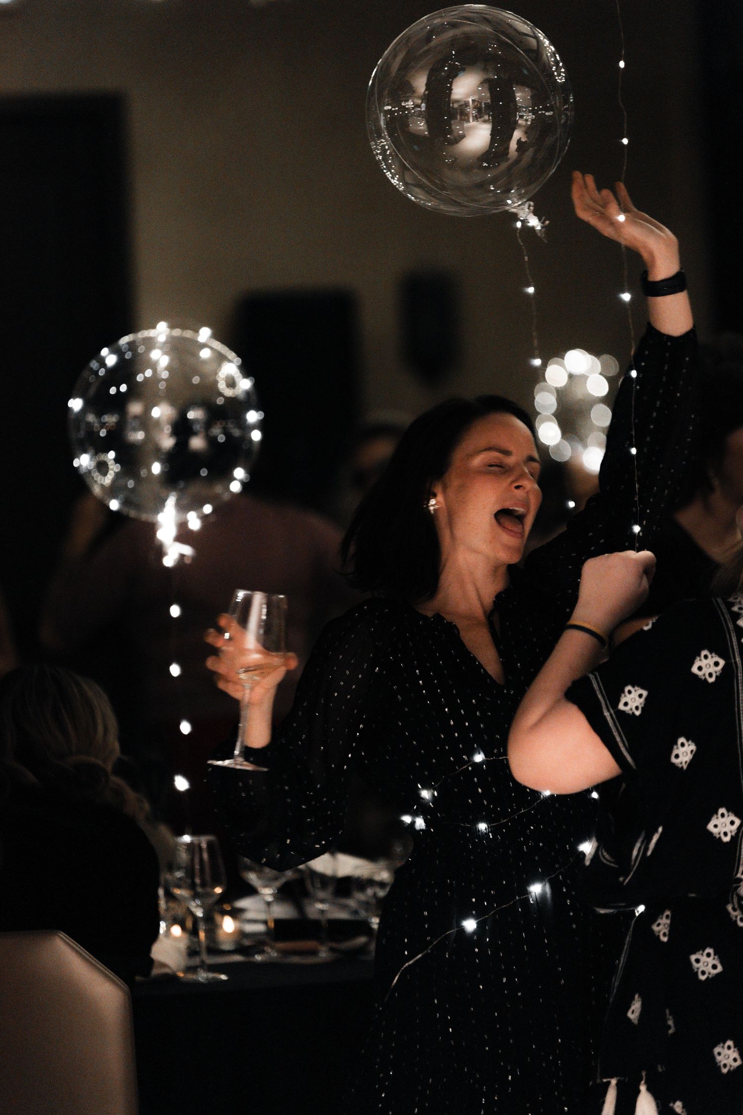 Person in sparkly dress celebrating with illuminated balloons and wine glass at a party.