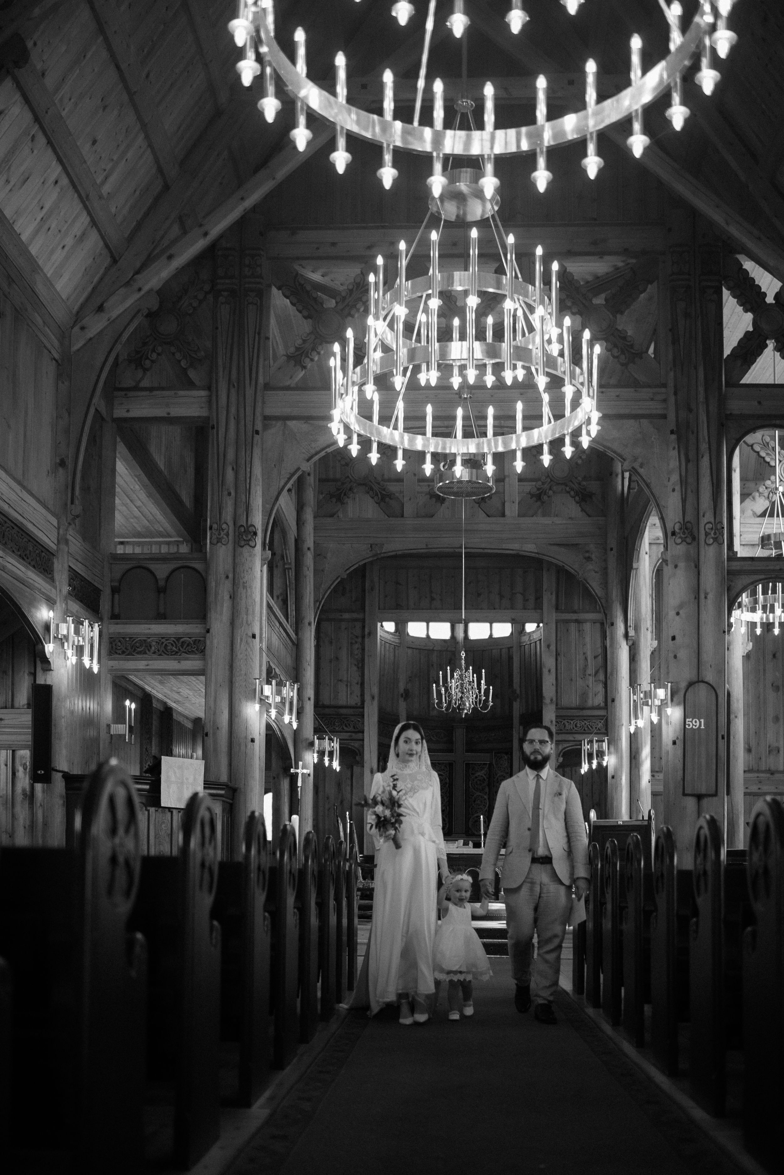 A black and white photo showing a wedding in a grand church with tiered chandeliers.