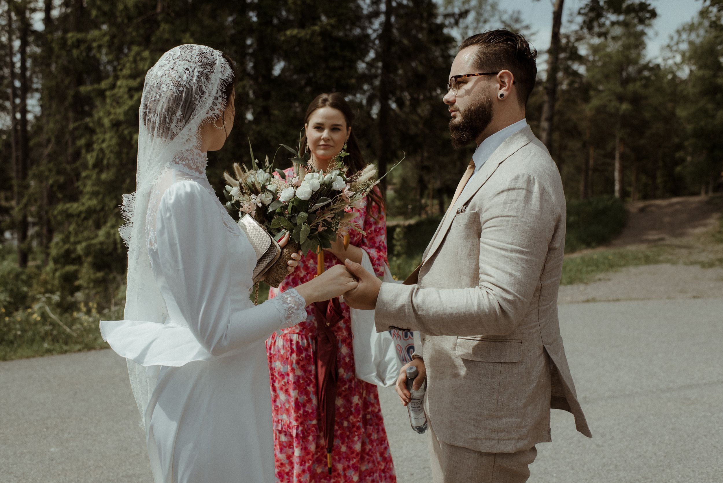 A wedding ceremony takes place outdoors with pine trees in the background.
