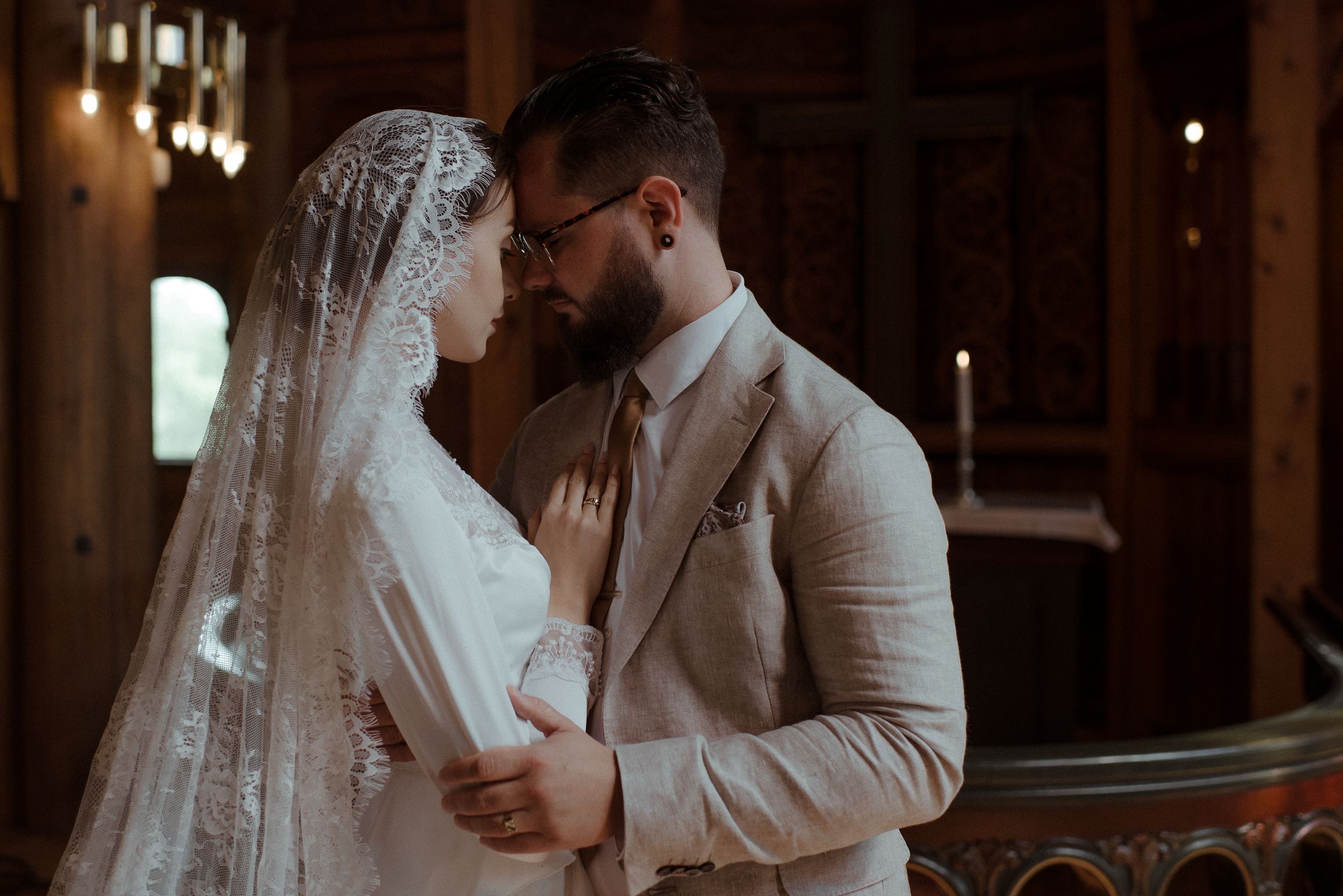 Intimate moment between newlyweds in a rustic wooden venue with warm lighting.