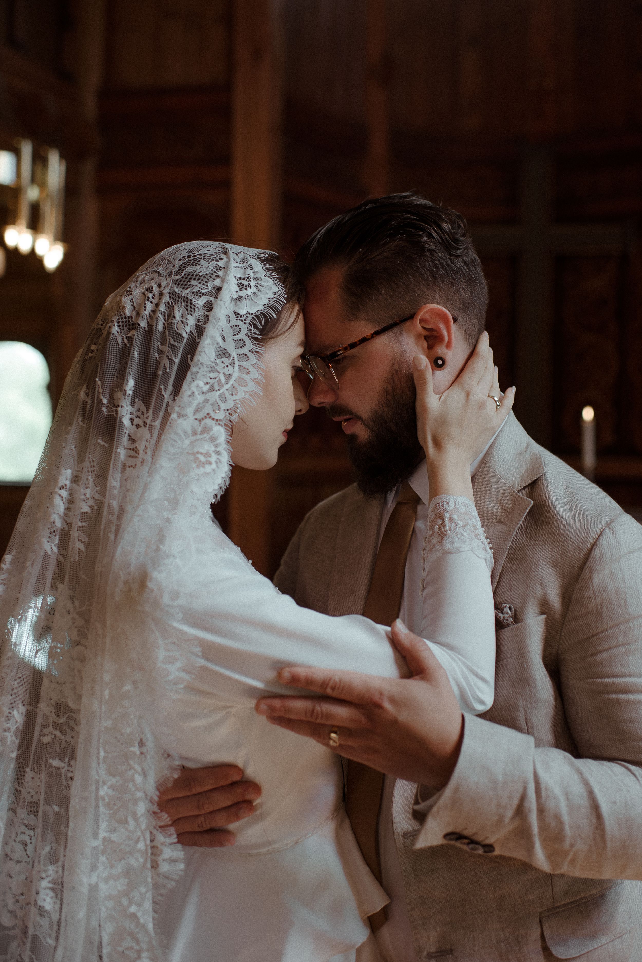 Tender embrace between newlyweds under soft lighting in a wooden interior setting.