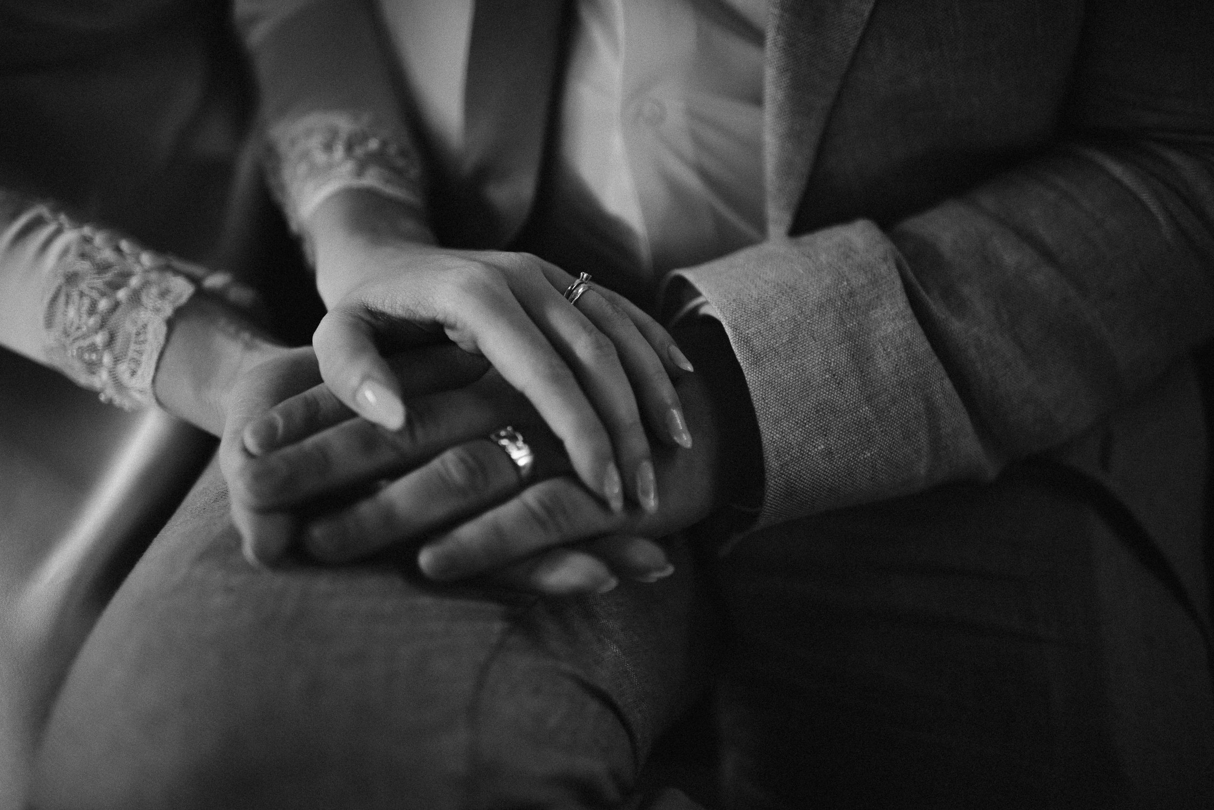 Close-up black and white shot of hands with wedding rings intertwined.