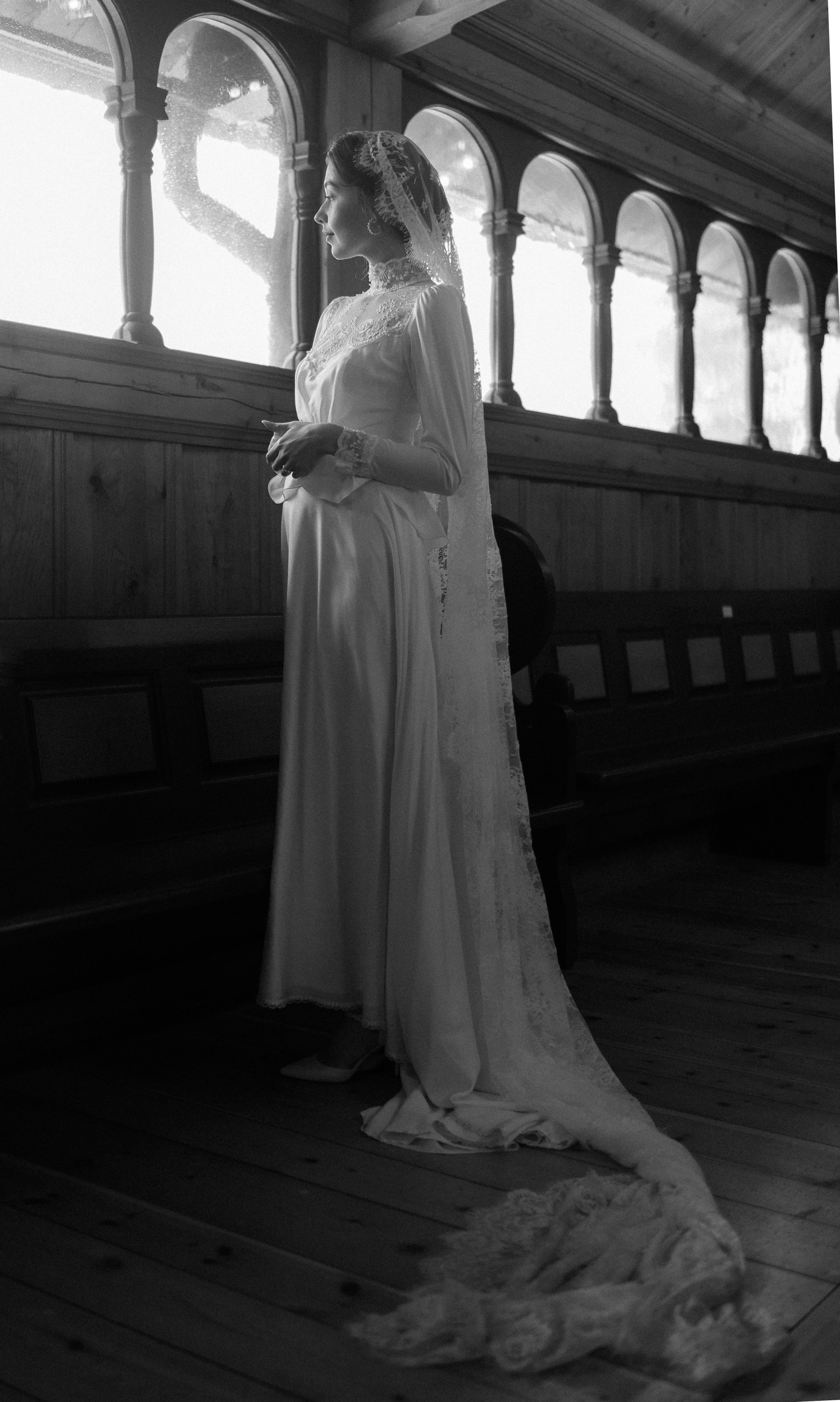A vintage black and white photo of a bride in a flowing gown with long train in a church hallway.
