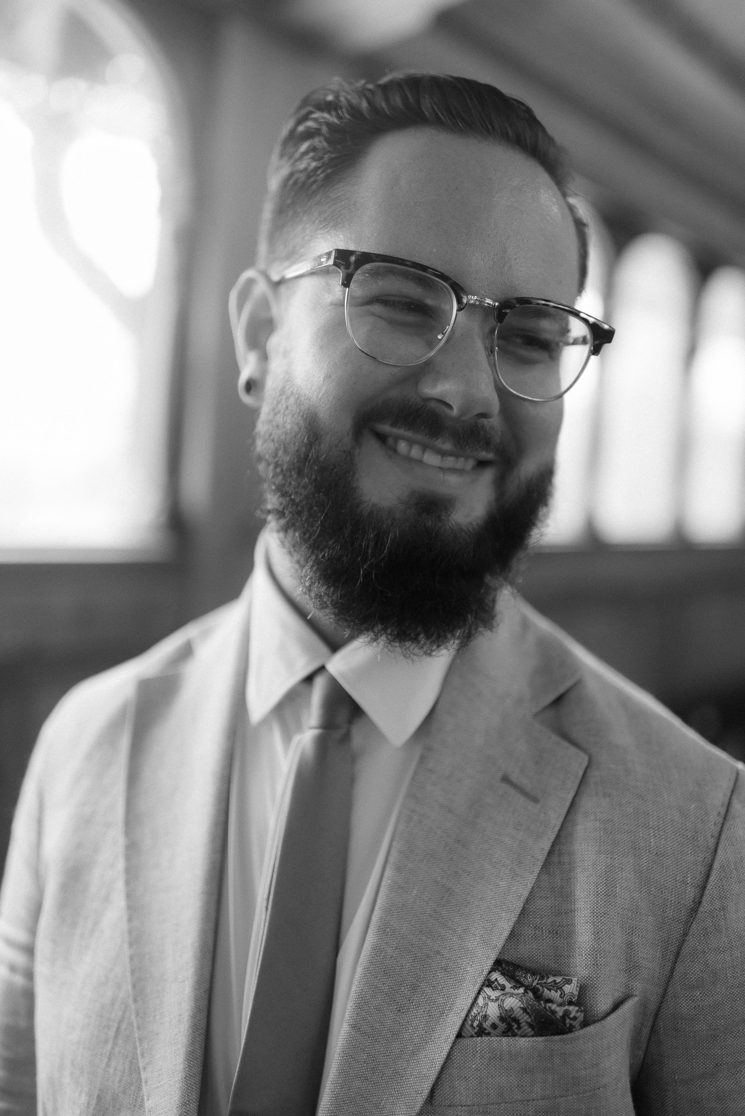Professional portrait in black and white of someone wearing a light colored suit and glasses.