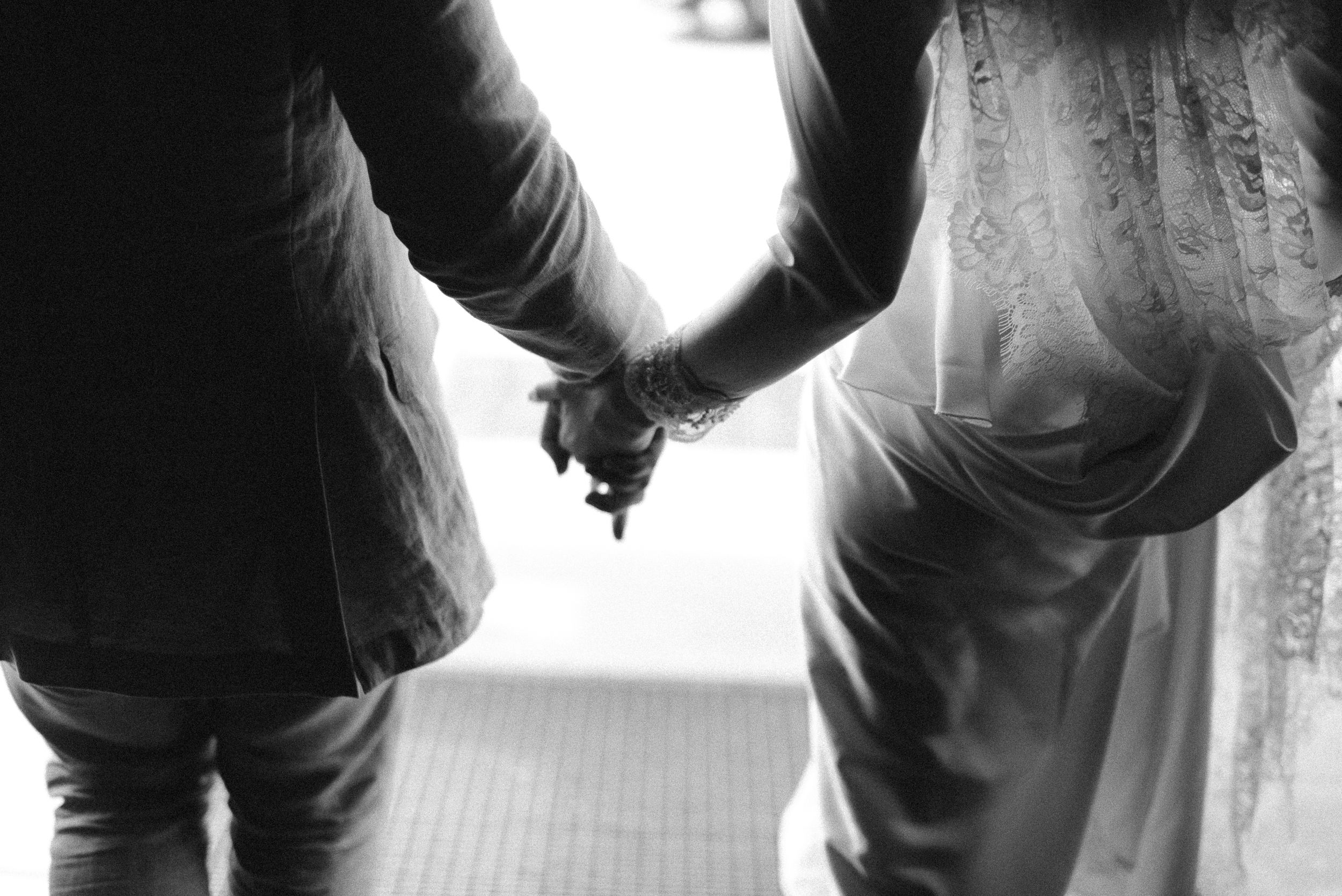 Black and white image of two people holding hands, showing formal attire.