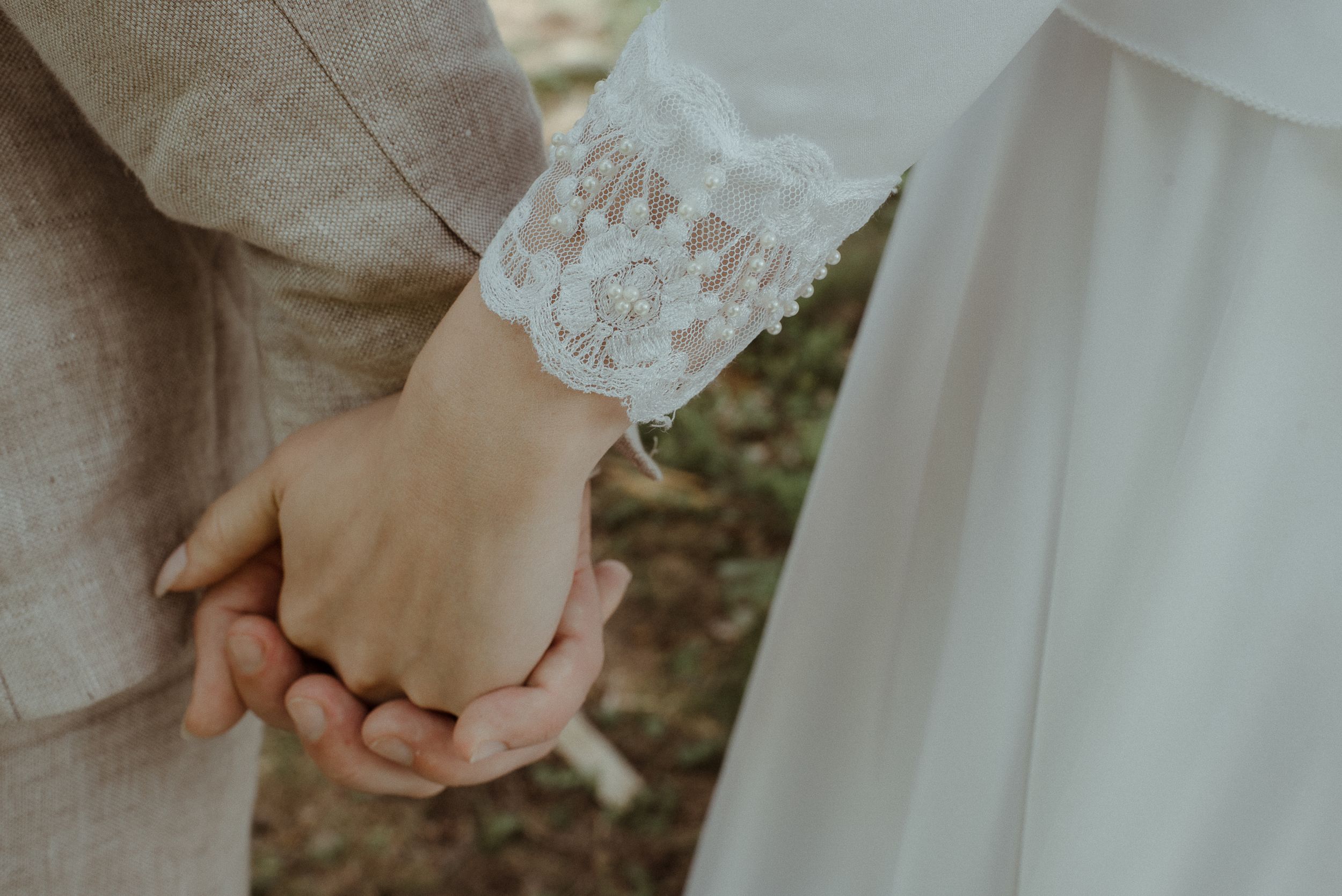 Close-up of newlyweds holding hands, showing lace sleeve detail of wedding dress.