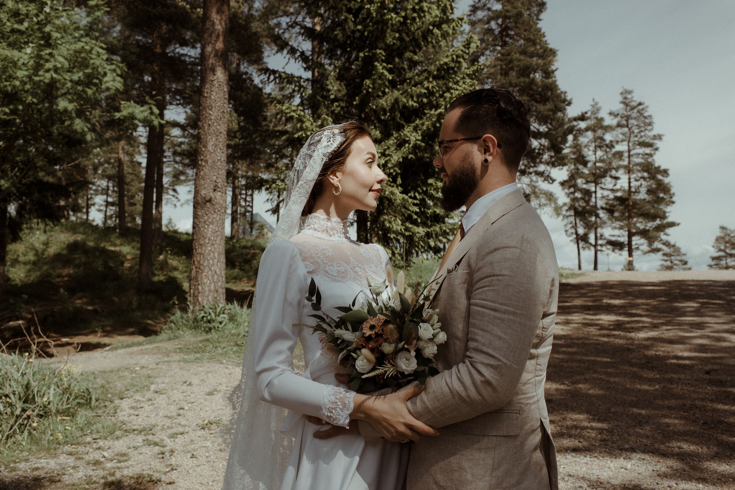 Wedding couple shares intimate moment while holding bouquet in sunlit forest setting.