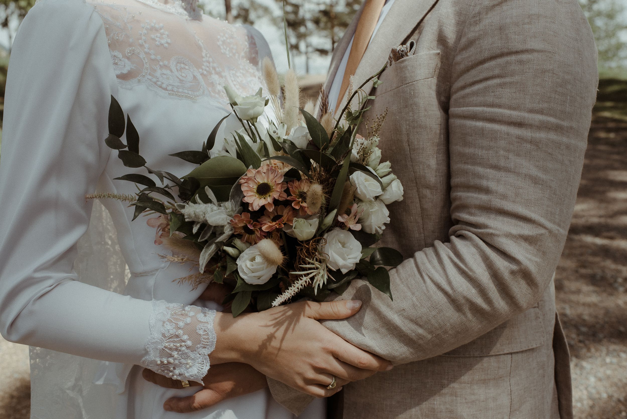 Close-up of couple holding beautiful wedding bouquet with white roses and greenery.