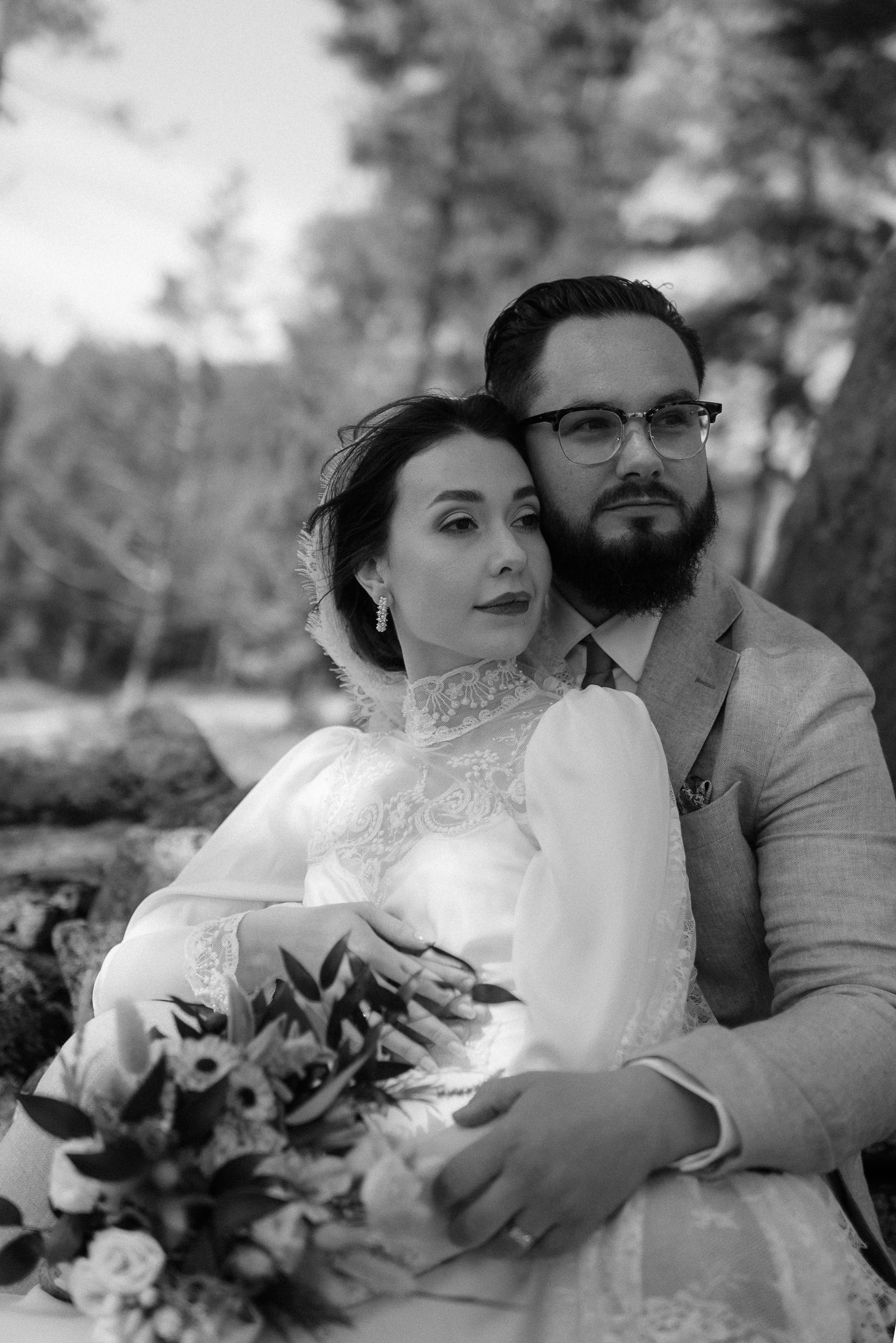 A romantic wedding portrait of a couple in vintage-inspired attire among pine trees.