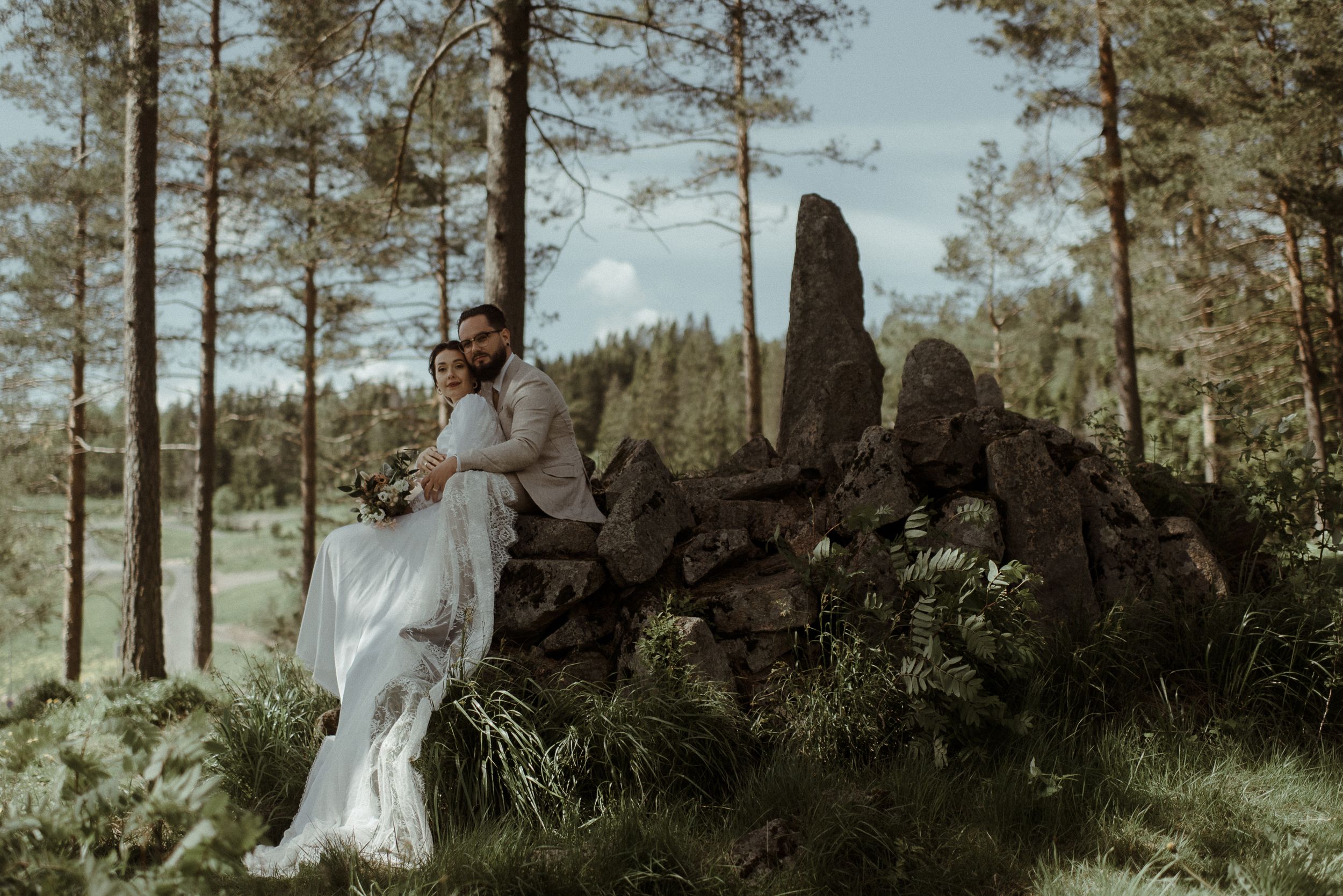 White-gowned figure stands near stone formation in a serene forest landscape.