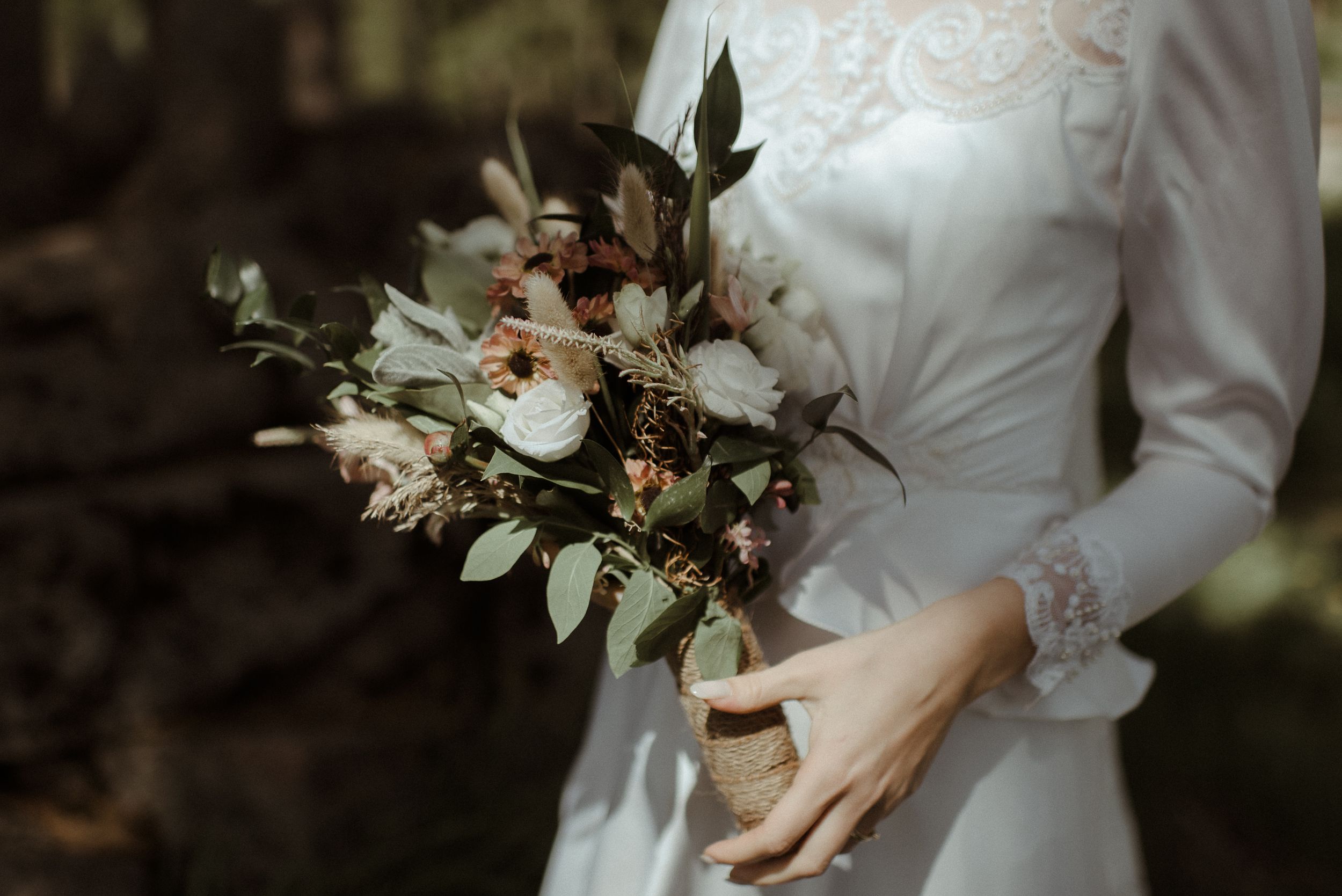 Close-up of bridal bouquet with white flowers and greenery against vintage wedding dress.