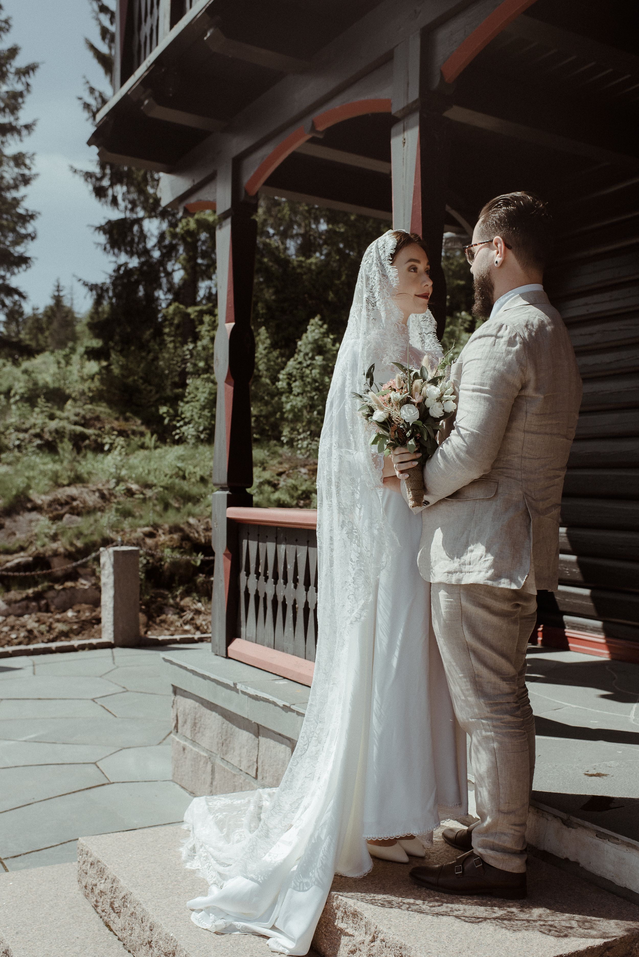 A romantic wedding moment captured on a rustic cabin porch with a flowing white veil.