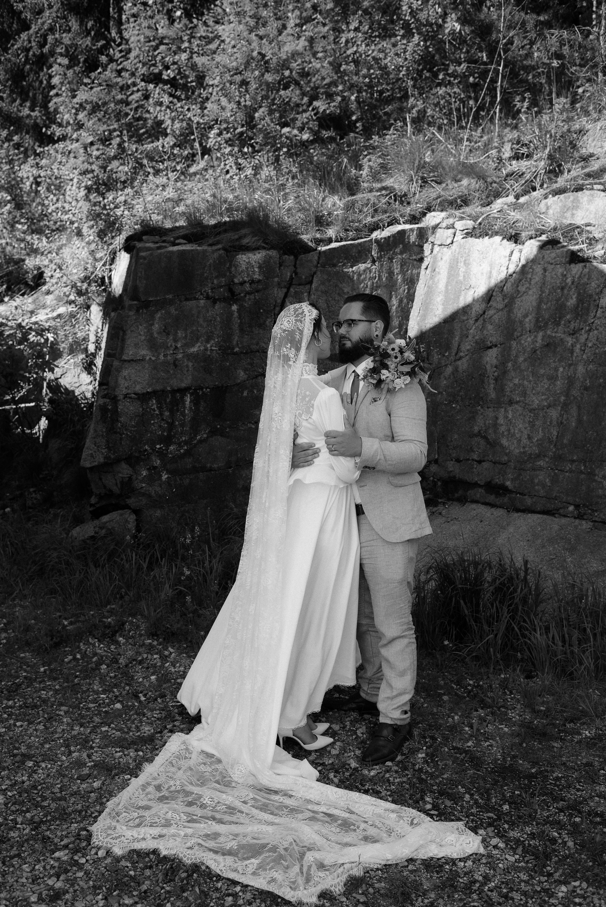 A black and white wedding portrait against a rocky wall backdrop in nature.